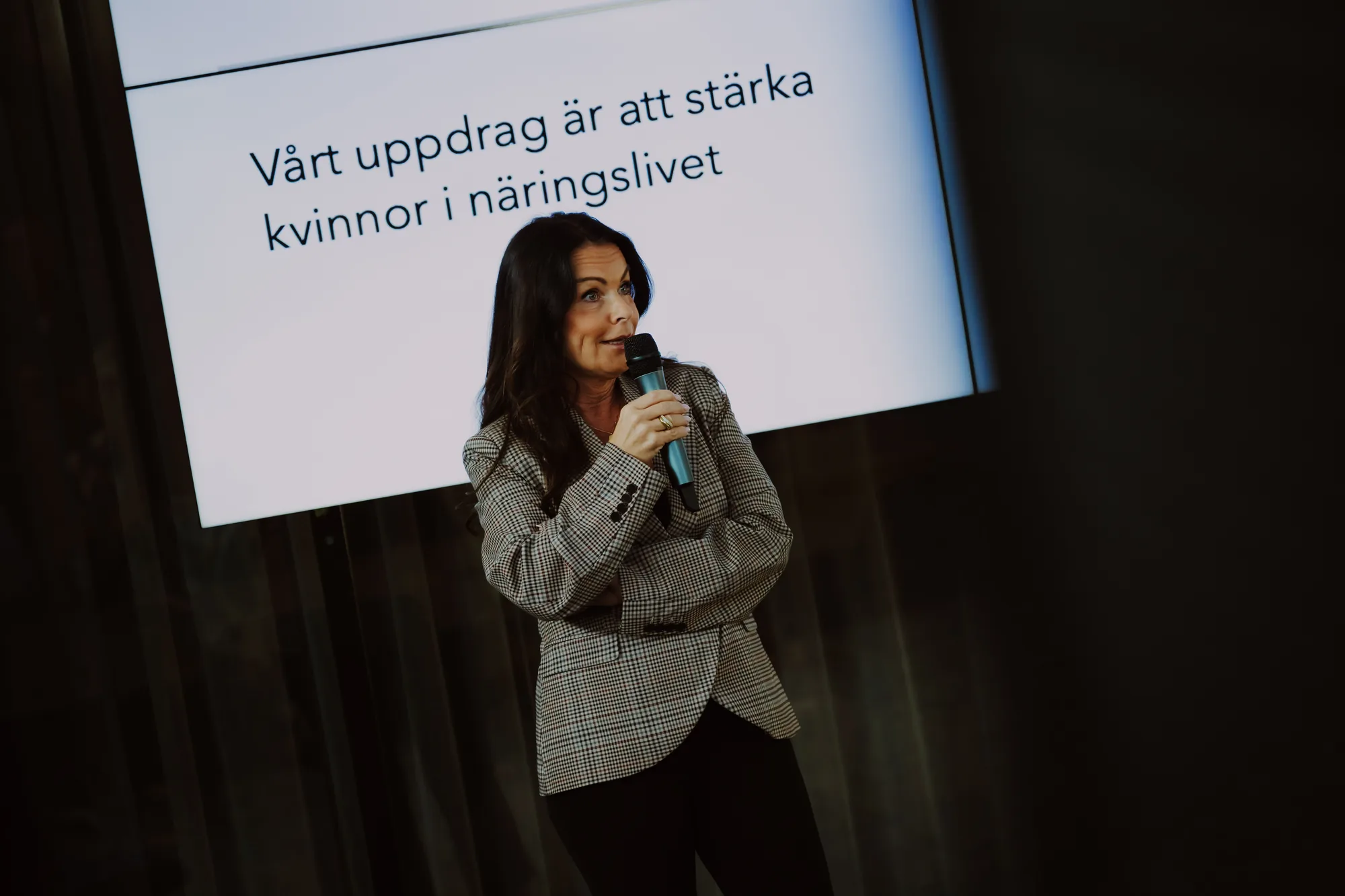 Talare med mikrofon framför texten om att stärka kvinnor i näringslivet